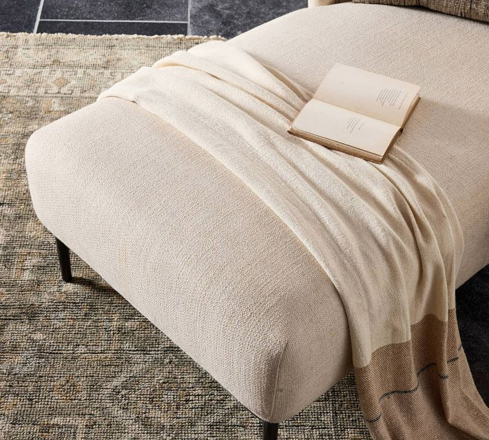 Top-down view of beige chaise lounge with cream blanket and open book draped on it