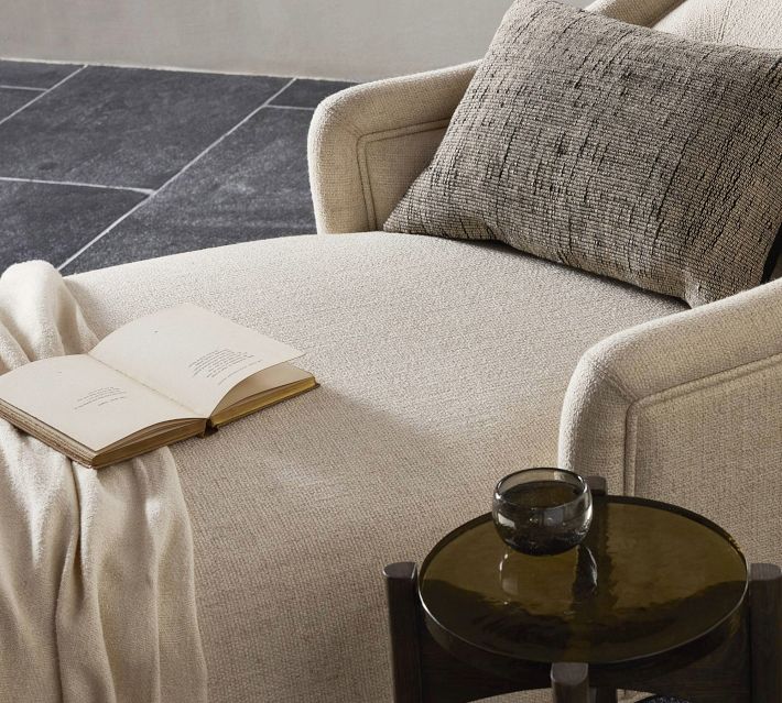Close-up of beige upholstered lounge chair with textured fabric and a patterned cushion, showing the arm and back