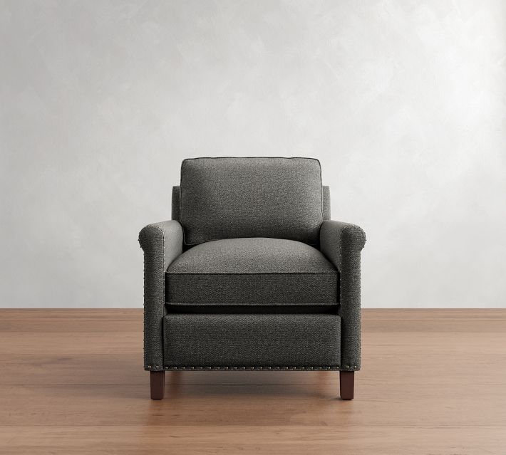 A dark gray upholstered armchair with wide arms and a boxed cushion, standing on wooden legs against a light textured wall.