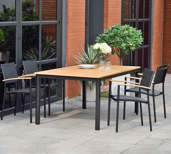 Outdoor dining area with a wooden table and black chairs placed on a patio near glass doors and plants