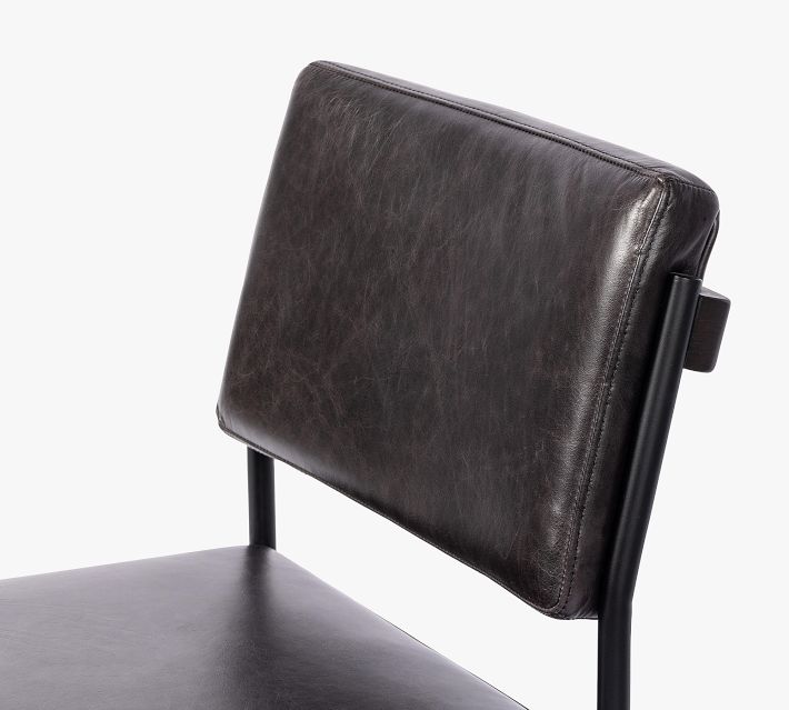 Close-up of black leather chair back with texture and stitching.