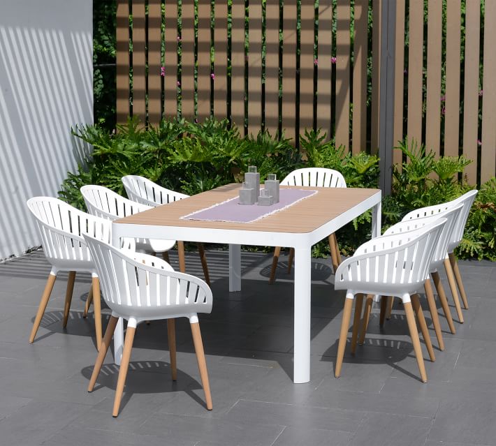 Rectangular wooden-top outdoor dining table with white legs, set in a garden