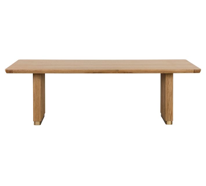 Long wooden dining table with two ribbed pedestal legs and brass base trim, shown on white background.