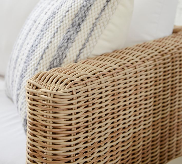 Close-up of tightly woven wicker armrest with beige cushion edge.