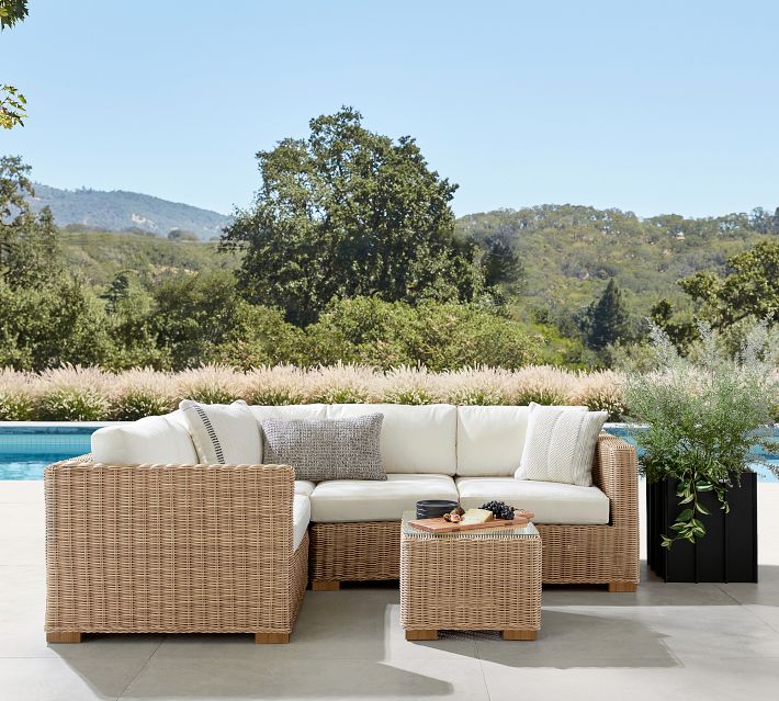 Wide outdoor seating arrangement with white cushions and wicker sofas by a pool.