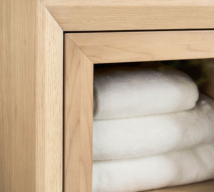 Inset view of the top corner of a wooden cabinet with glass door showing folded white towels inside.