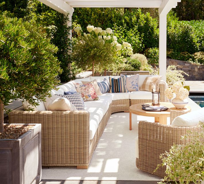 Outdoor living space with white pergola and cushioned rattan sectional facing a pool.