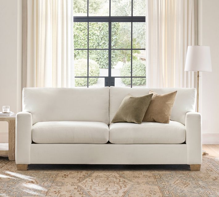 White sofa with two-seater, pillows, and large window behind