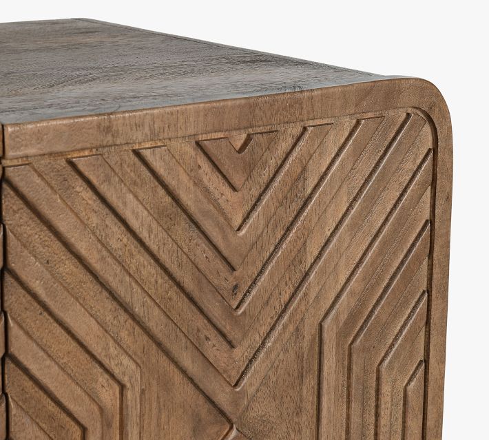 Close-up of a wooden cabinet door with an angular chevron geometric carved pattern