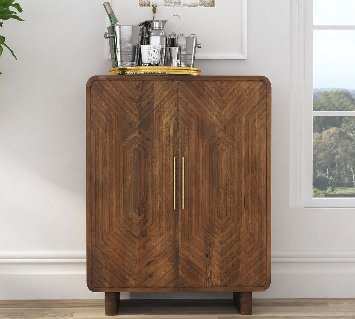 A wooden cabinet with geometric carved doors and brass handles, topped with a metal tray of barware