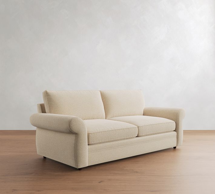 Beige two-seat sofa with rolled arms and cushions, shown from a three-quarter angle.