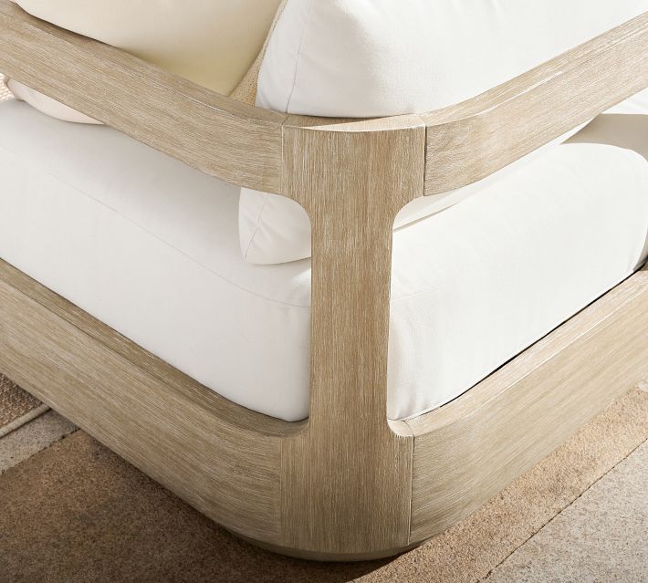 Corner of a wooden armchair with white cushions, showing curved wood joints
