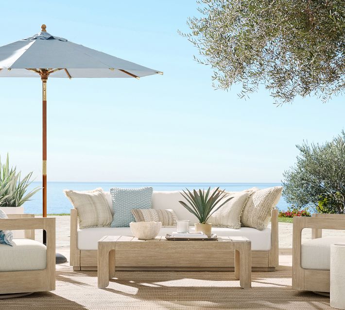 Outdoor seating area with sofa, cushions, and a distant sea view under a blue sky