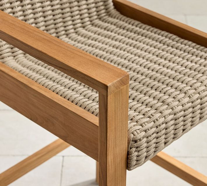Corner detail of the wooden armrest and woven rope seating on an outdoor chair.