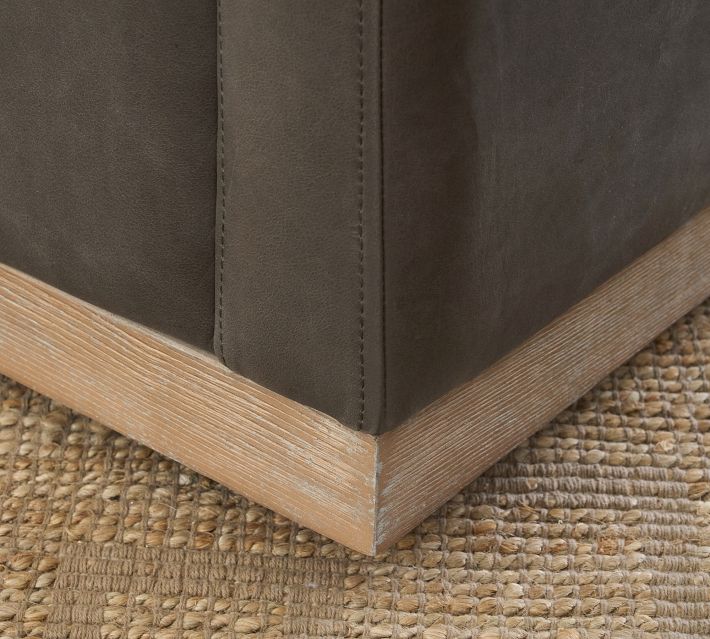 Lower corner of the armchair with visible seam and wooden base edge on a textured rug.