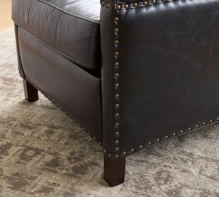 Bottom corner of black leather chair with studded trim and wooden leg.