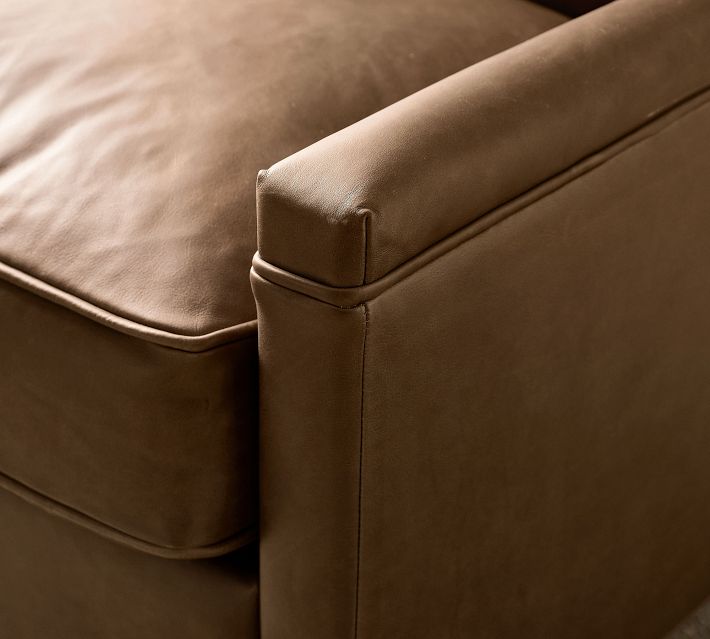 Corner of brown leather chair showing stitched piping and armrest.