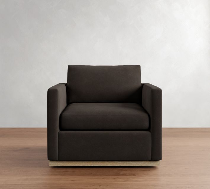 Single dark brown armchair with thick cushions on a wooden base against a plain light wall.