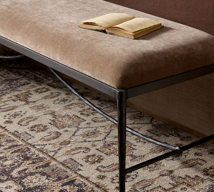 Close-up of the upholstered bench showing a brown velvet-like cushion and a dark metal frame with a curved crossbar.