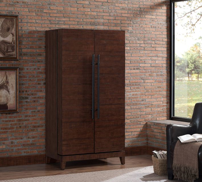 Tall wooden armoire/wardrobe with double doors in a brick-walled living space.